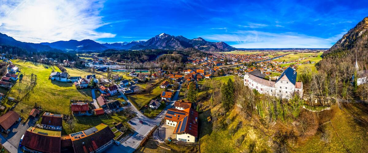 A panoramic view of a town nestled between mountains, with a prominent castle and a river running through the center.