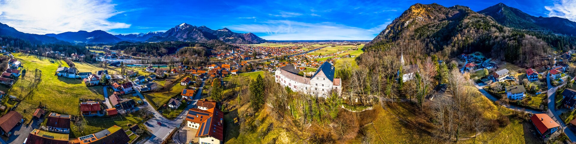 A panoramic view of a town nestled between mountains, with a prominent castle and a river running through the center.