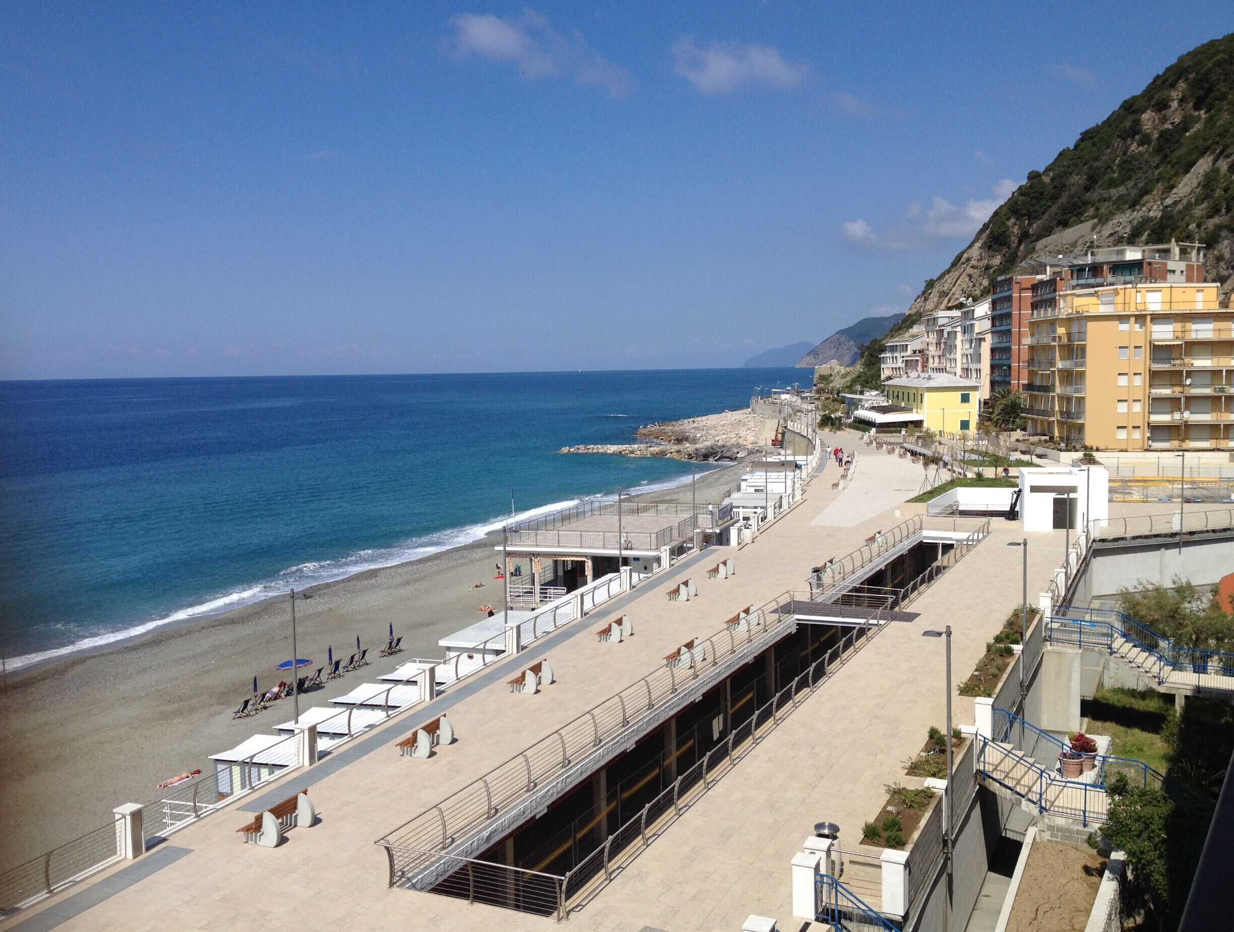 A coastal promenade with a beach, a rocky shoreline, and buildings along the cliff.