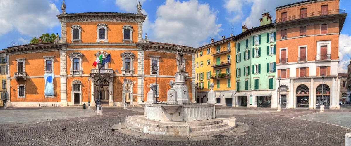 A historic square with a fountain, a statue, and colorful buildings.