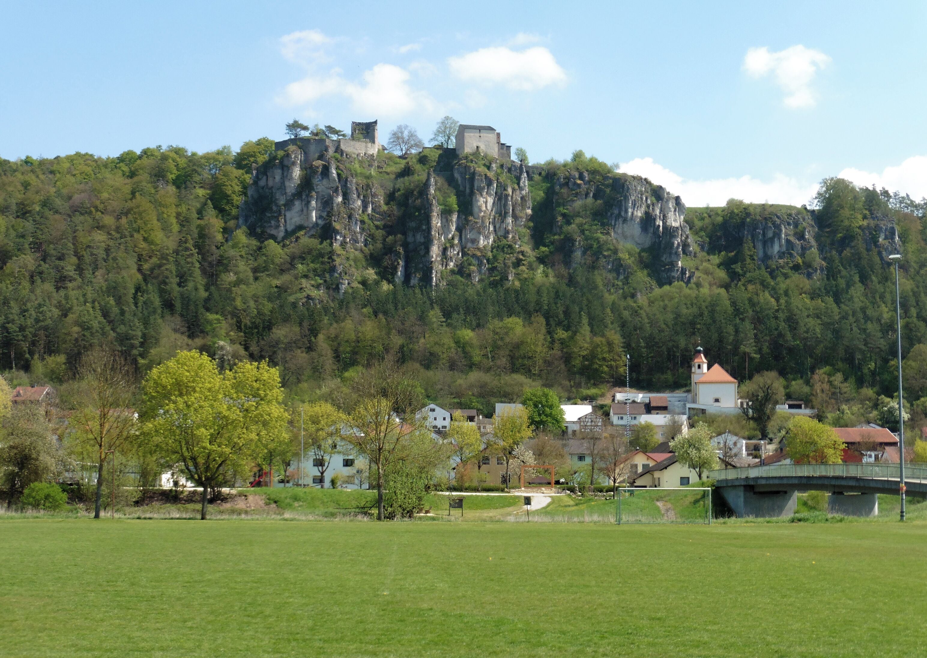 Eine Stadt mit Gebäuden im Vordergrund und einer Burg auf einem Felsen im Hintergrund.