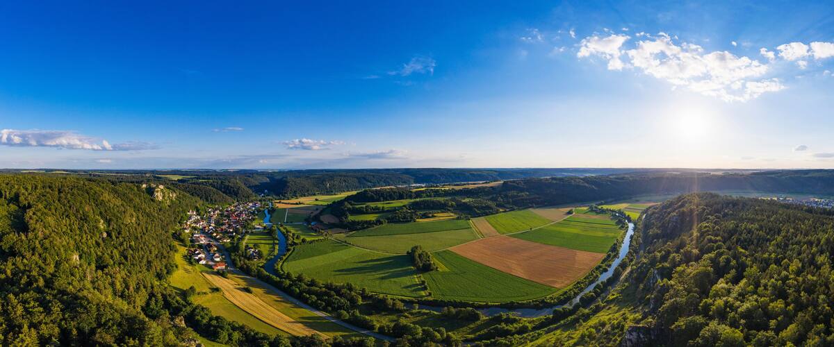 A panoramic view of a rural landscape with a river, fields, and a small village.