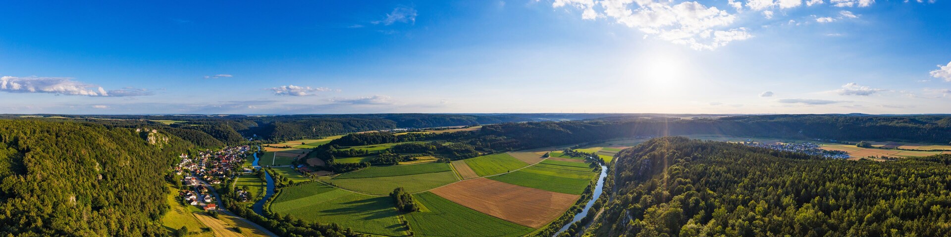 A panoramic view of a rural landscape with a river, fields, and a small village.