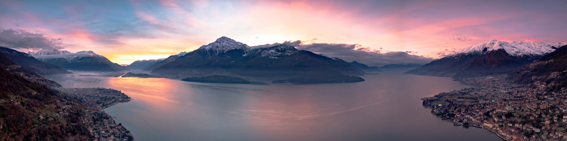 A mountainous landscape with a calm lake, snow-capped peaks, and a town along the water's edge.