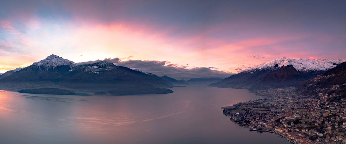 A mountainous landscape with a calm lake, snow-capped peaks, and a town along the water's edge.