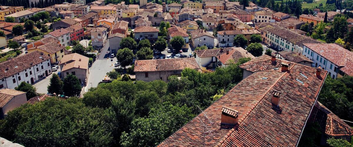 A historic town with terracotta-roofed buildings, a river, and surrounding green fields.