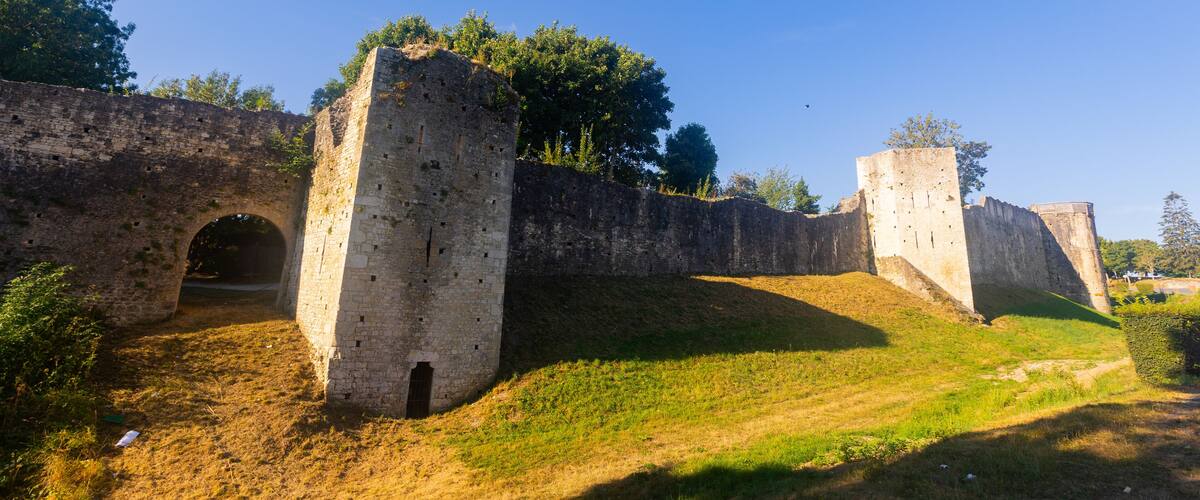 A historical stone wall with a small archway and a grassy hill.