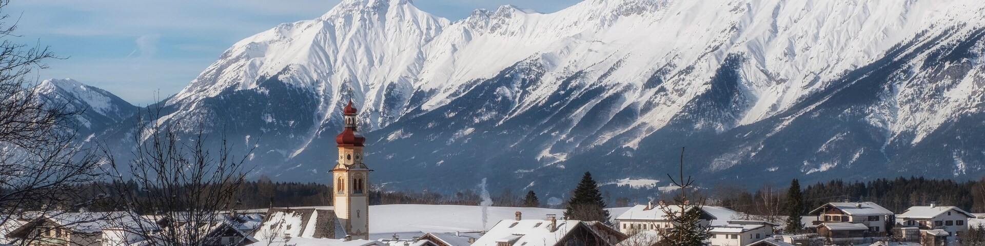 Uma aldeia coberta de neve, com uma igreja e montanhas ao fundo.