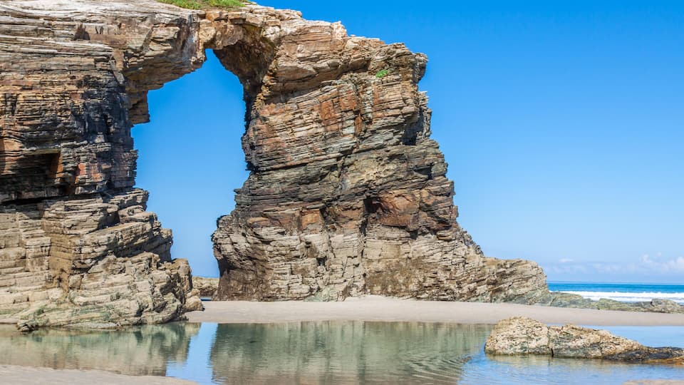 A rock formation with a natural arch over a beach.
