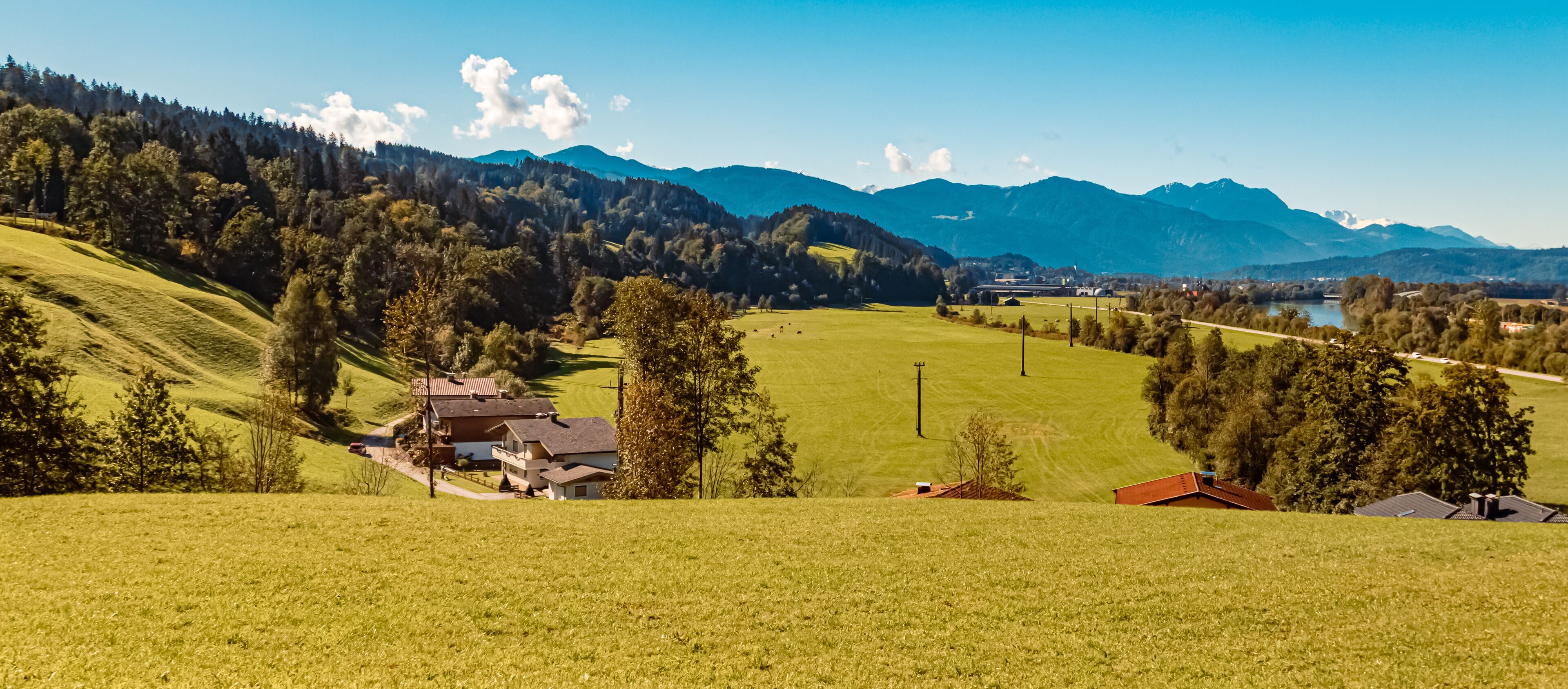A rural landscape with rolling hills, a house, and distant mountains.
