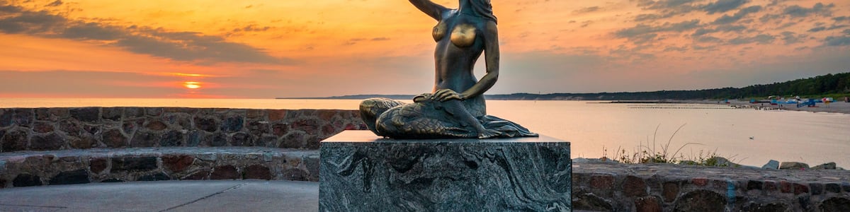 A statue of a woman on a pedestal by a waterfront during sunset.