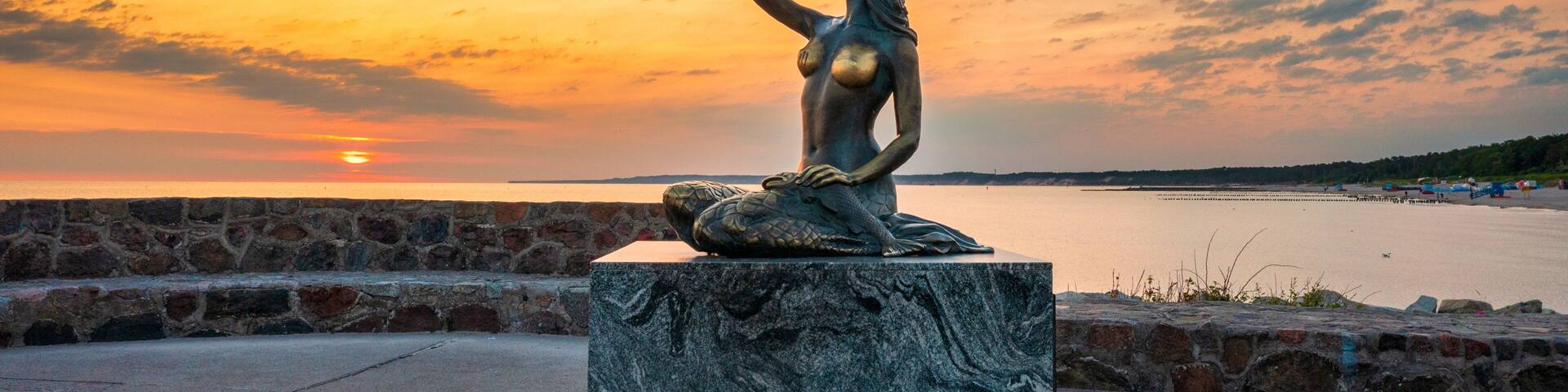 A statue of a woman on a pedestal by a waterfront during sunset.