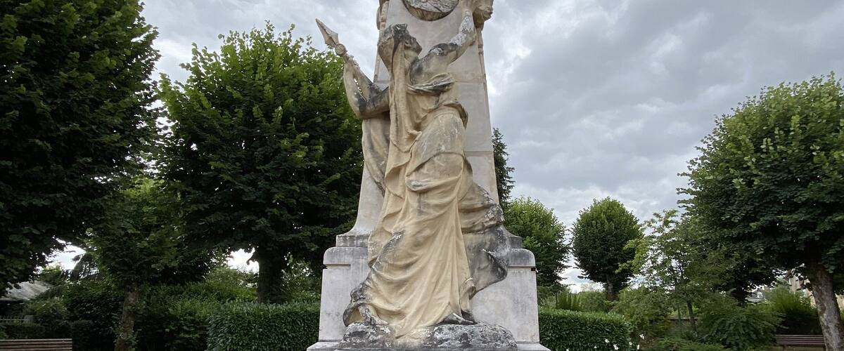 A statue of Corbigny with inscriptions, surrounded by colorful flowers and trees.