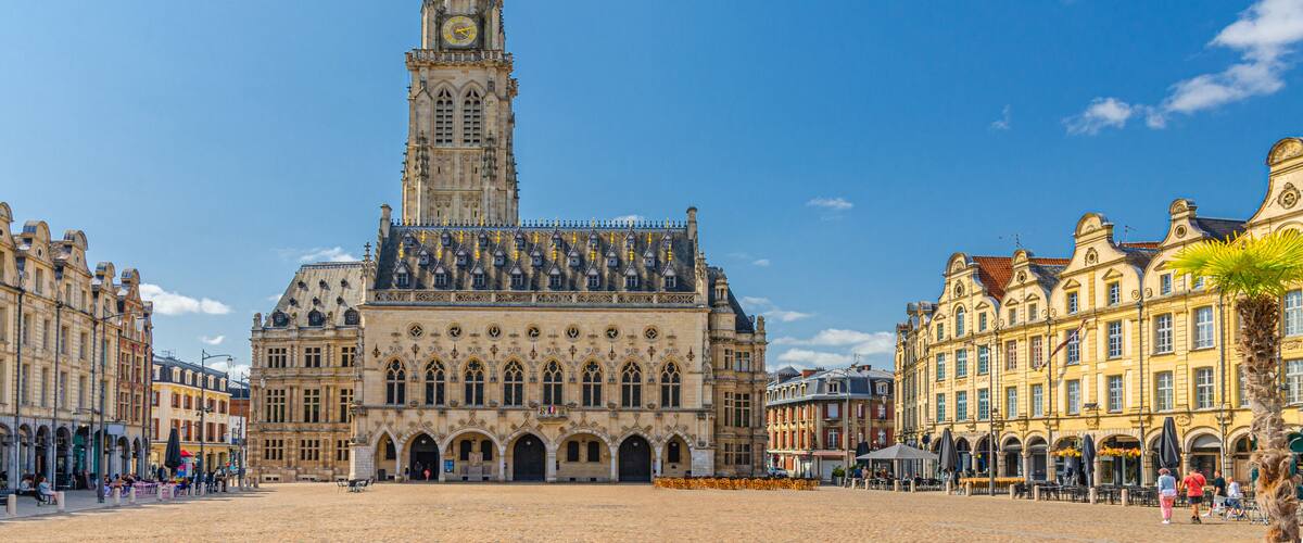 A historic building with a tall tower, a large open square, and surrounding classic architecture.