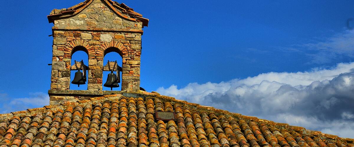 A bell tower with a cross on top, surrounded by clouds.