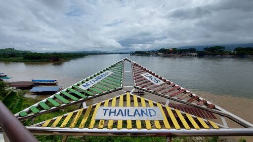 Un río con barcos y un puente adornado con banderas de Myanmar, Laos y Tailandia.