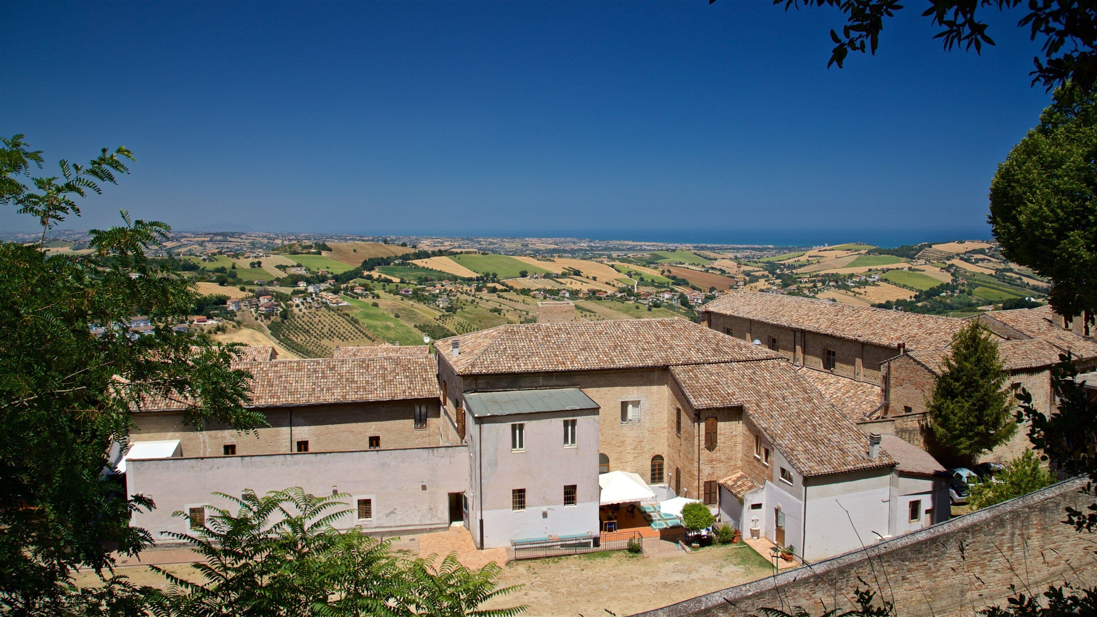 A village with terracotta-roofed buildings, a clear blue sky, and rolling hills in the background.