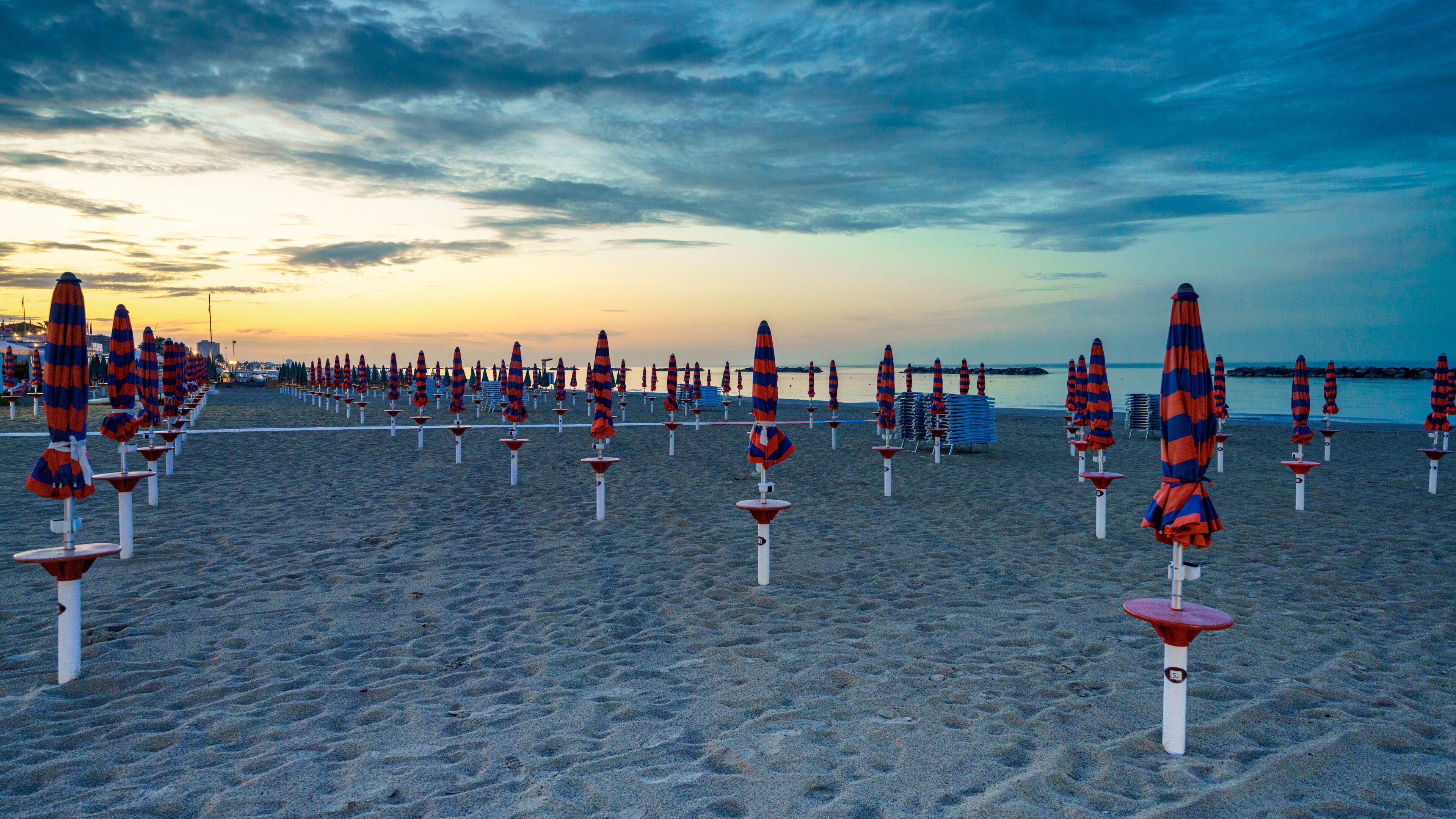 Una playa con hileras de sombrillas y sillas a rayas.
