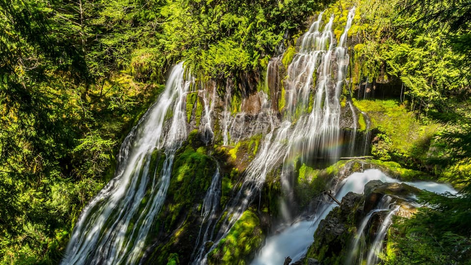 A multi-tiered waterfall surrounded by dense green forest.