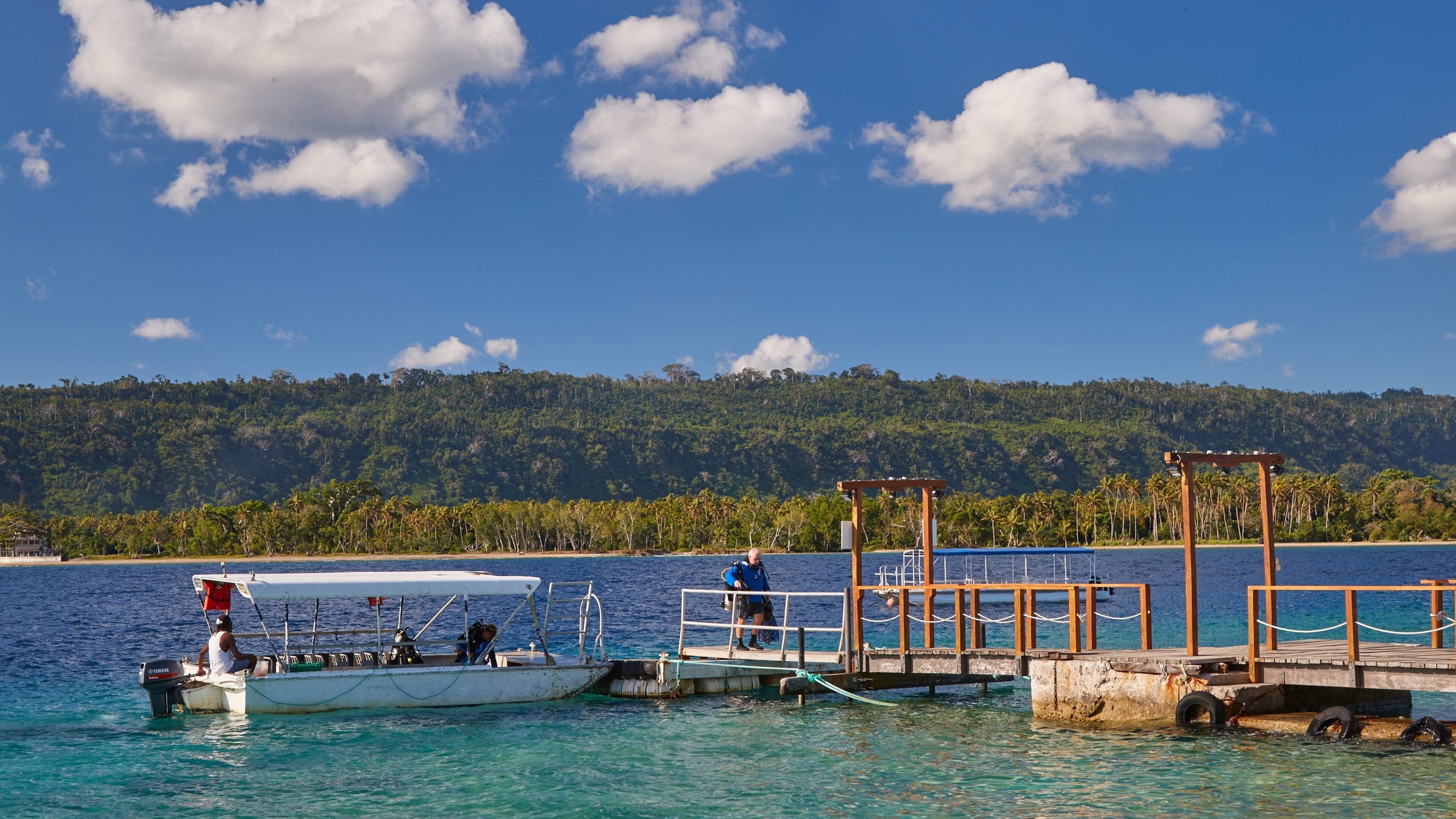 A boat docked at a pier with a forested island in the background.