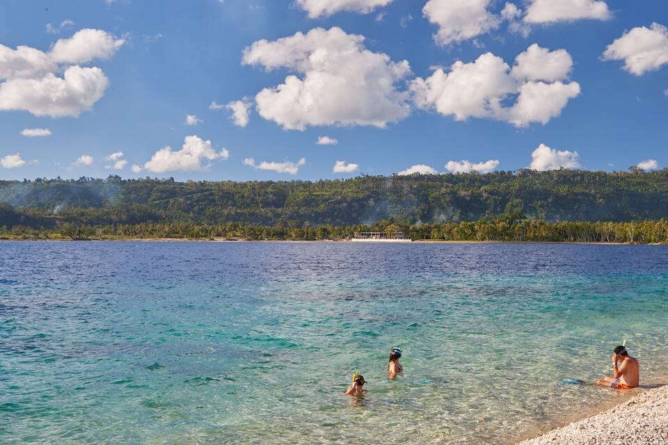 A clear blue sea with people swimming and sunbathing on a sandy beach.