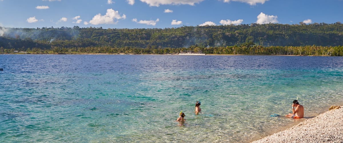 A clear blue sea with people swimming and sunbathing on a sandy beach.