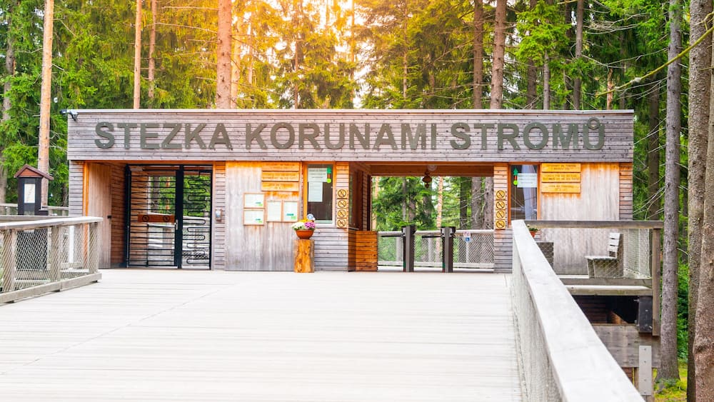 Ein hölzernes Gebäude mit einem Schild, auf dem 'STEZKA KORUNAMI STROMO' steht, inmitten eines bewaldeten Gebiets.