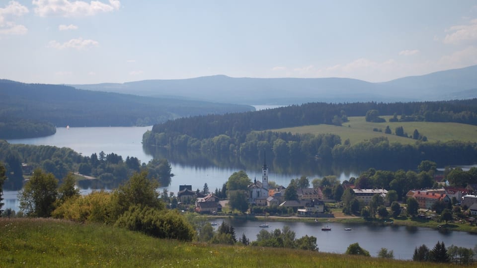 A lakeside village with a church, surrounded by hills and dense forests.