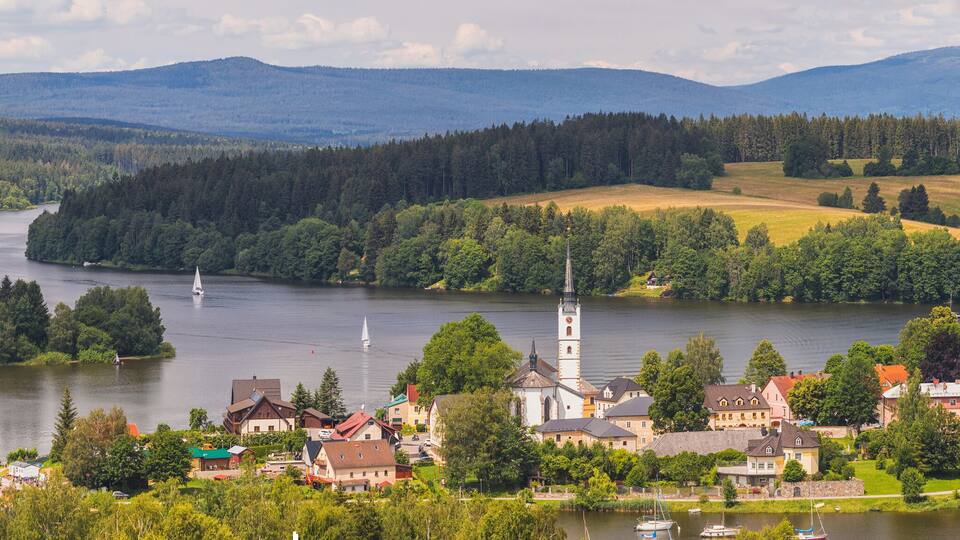 A lakeside town with a church, sailboats, and surrounding hills.