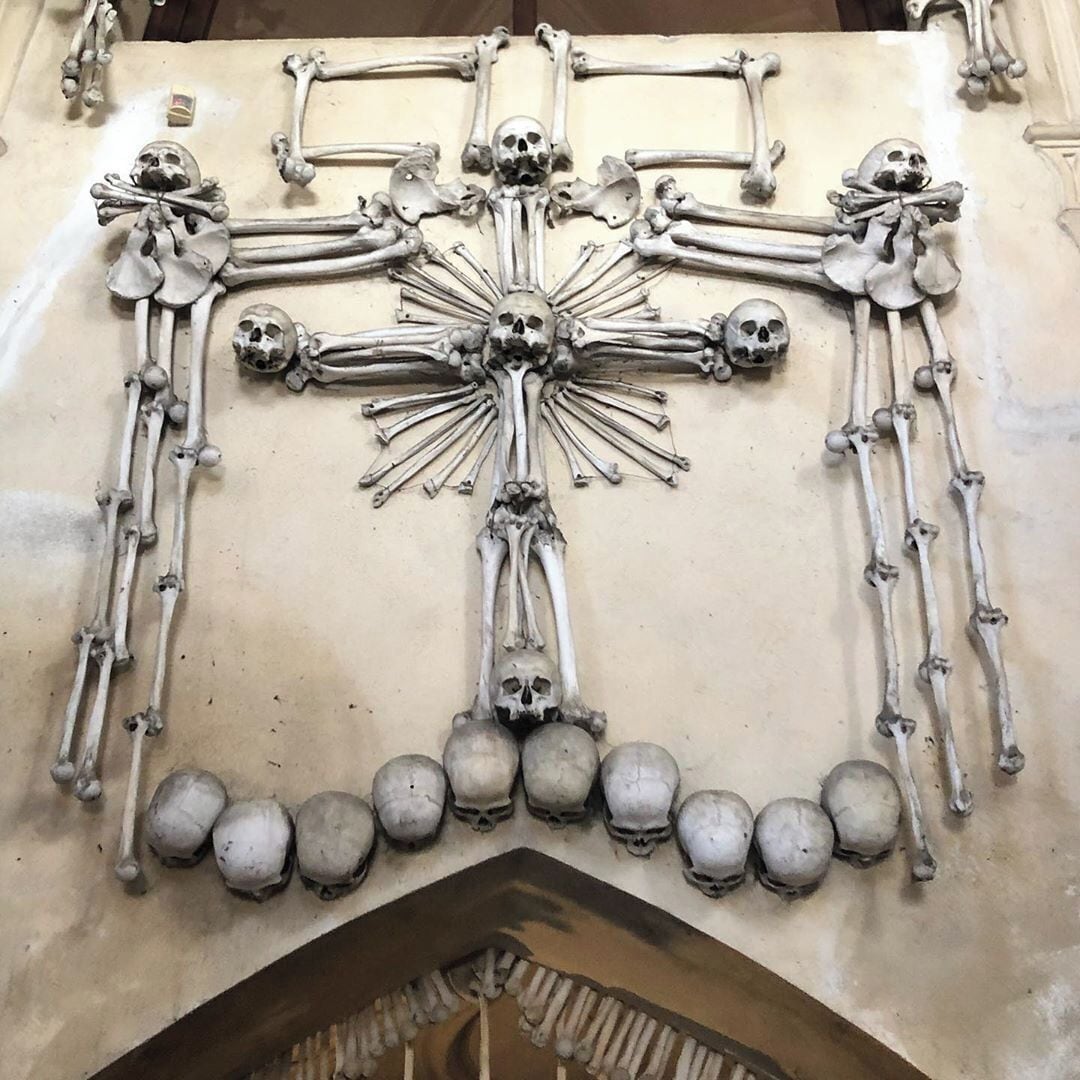 The Sedlec Ossuary is located beneath the Cemetery Church of All Saints in the Czech Republic. Its origin story is a long one, beginning with an abbot in 1278 who sprinkled dirt from the Holy Land over the Sedlec cemetery. This act prompted a huge influx of people who wanted to be laid to rest there. The cemetery's popularity, as well as factors such as wars and the Black Plague, caused an excess of bodies to be delivered and buried. Skeletons were exhumed and stacked over time in the chapel beneath the church. In 1870, a woodcarver named František Rint was hired to organize the skeletons, and he created the macabre designs that now make up the ossuary.
#History