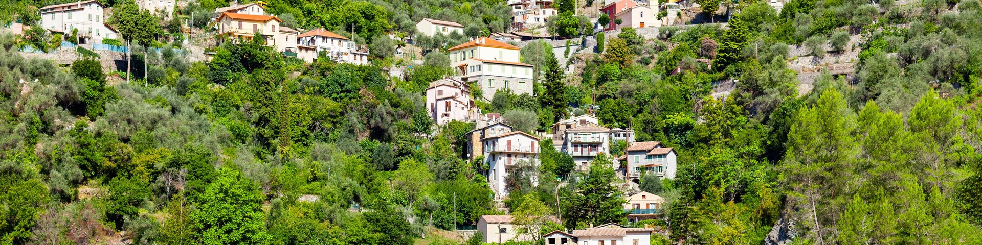 Un pueblo en la ladera de una colina con casas construidas en la pendiente, rodeado de densa vegetación verde y una montaña al fondo.