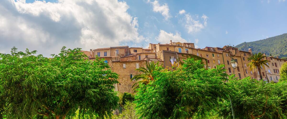 A historic town with terracotta-roofed buildings, lush greenery, and a mountainous backdrop.