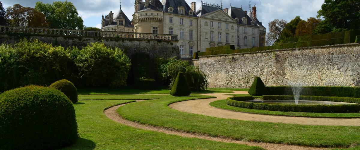 A grand château with a formal garden, including neatly trimmed hedges and a fountain.