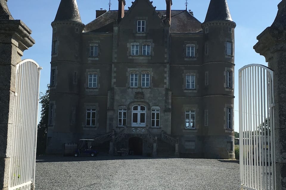 A large, historic building with multiple towers and a gravel driveway.