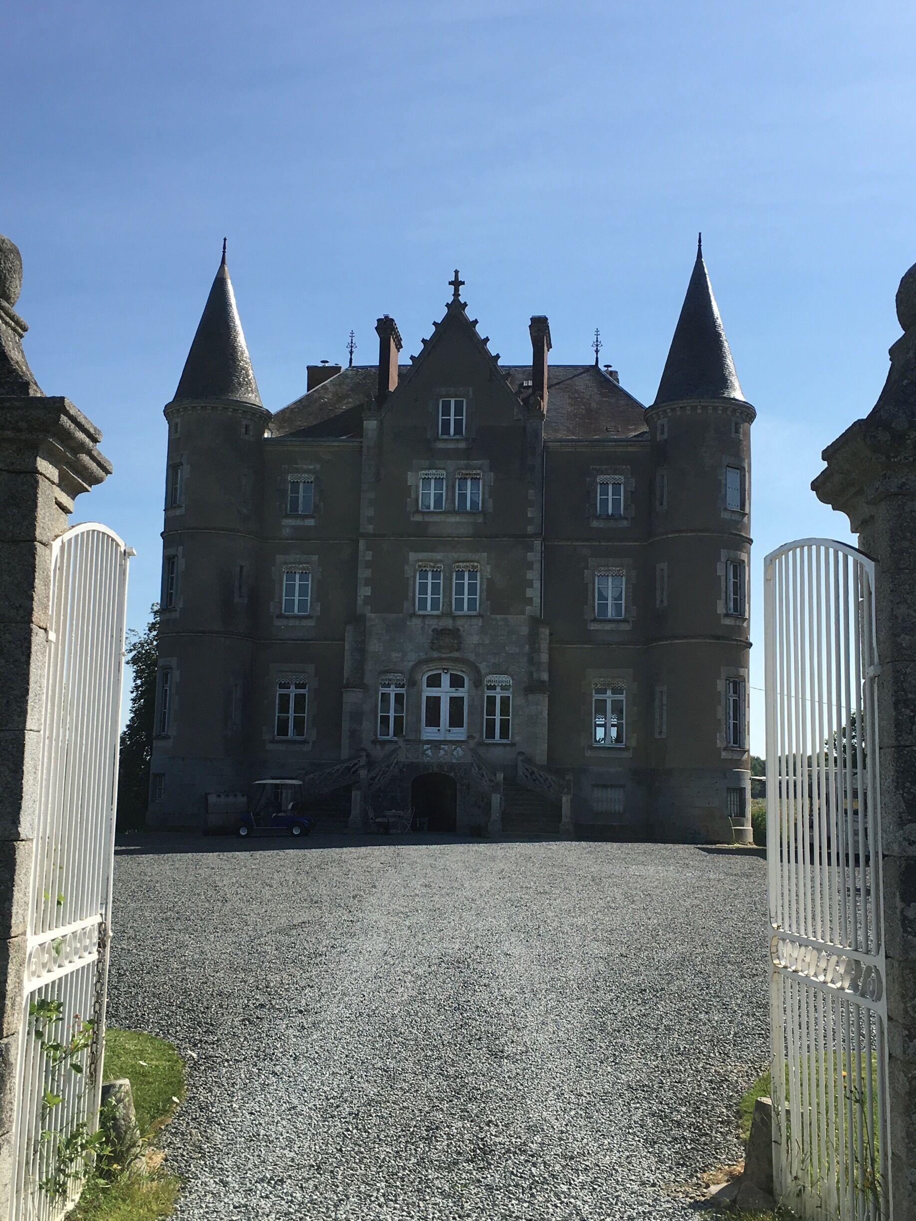 A large, historic building with multiple towers and a gravel driveway.