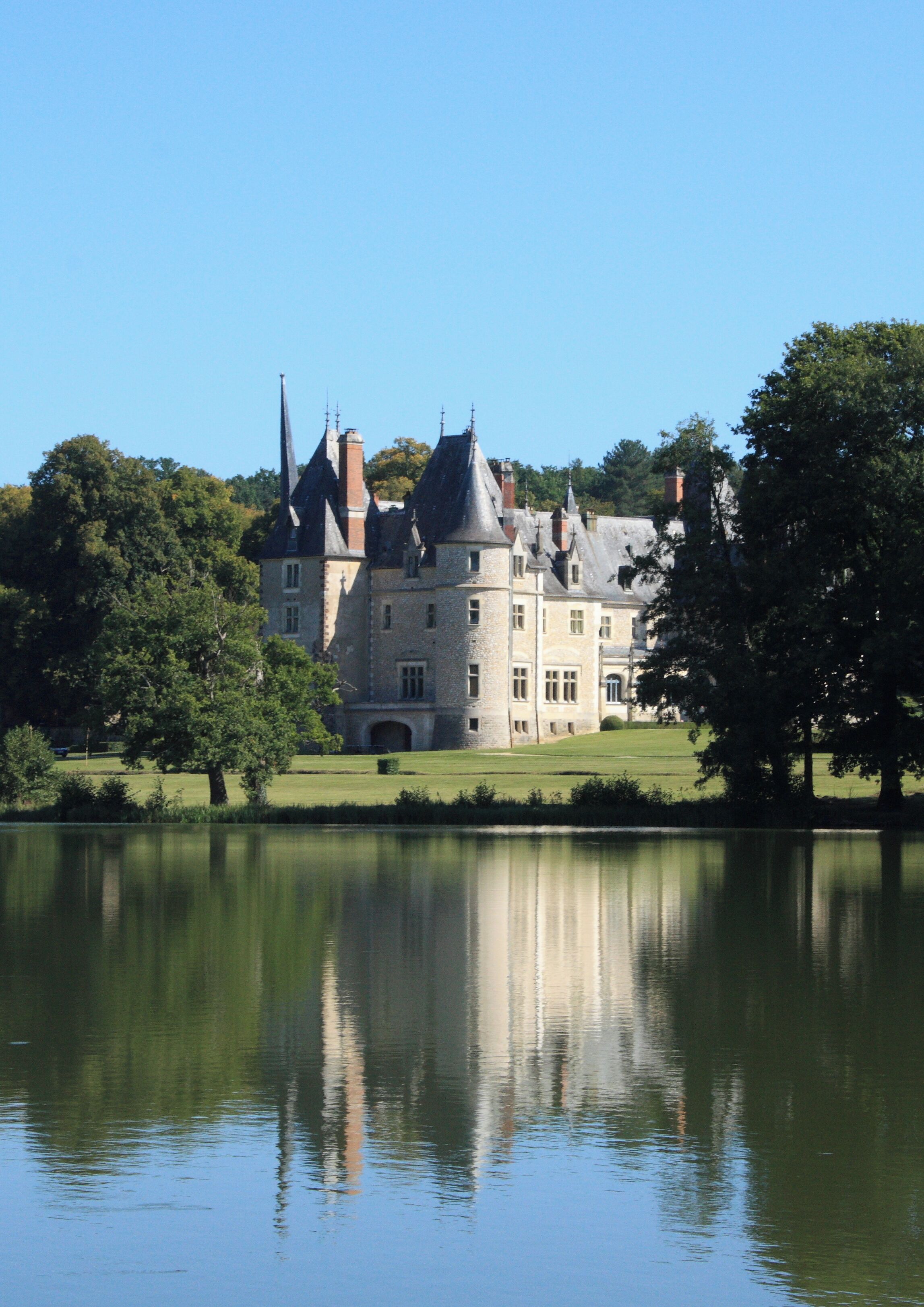 A large, historic castle with multiple towers, surrounded by a lake and lush greenery.