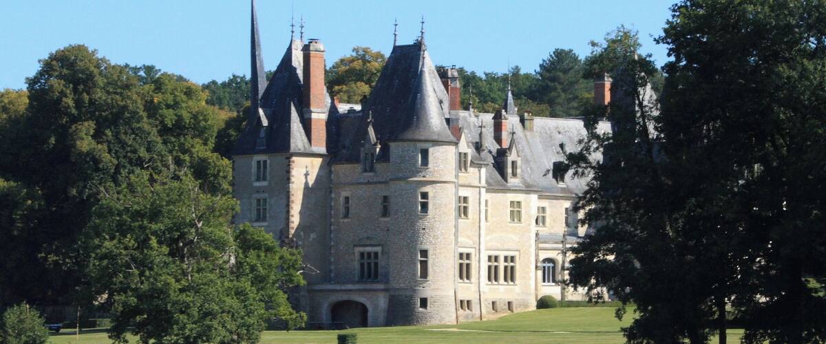 A large, historic castle with multiple towers, surrounded by a lake and lush greenery.