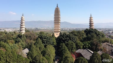 Tres torres de estilo pagoda en medio de un área boscosa, con un paisaje urbano distante y montañas.