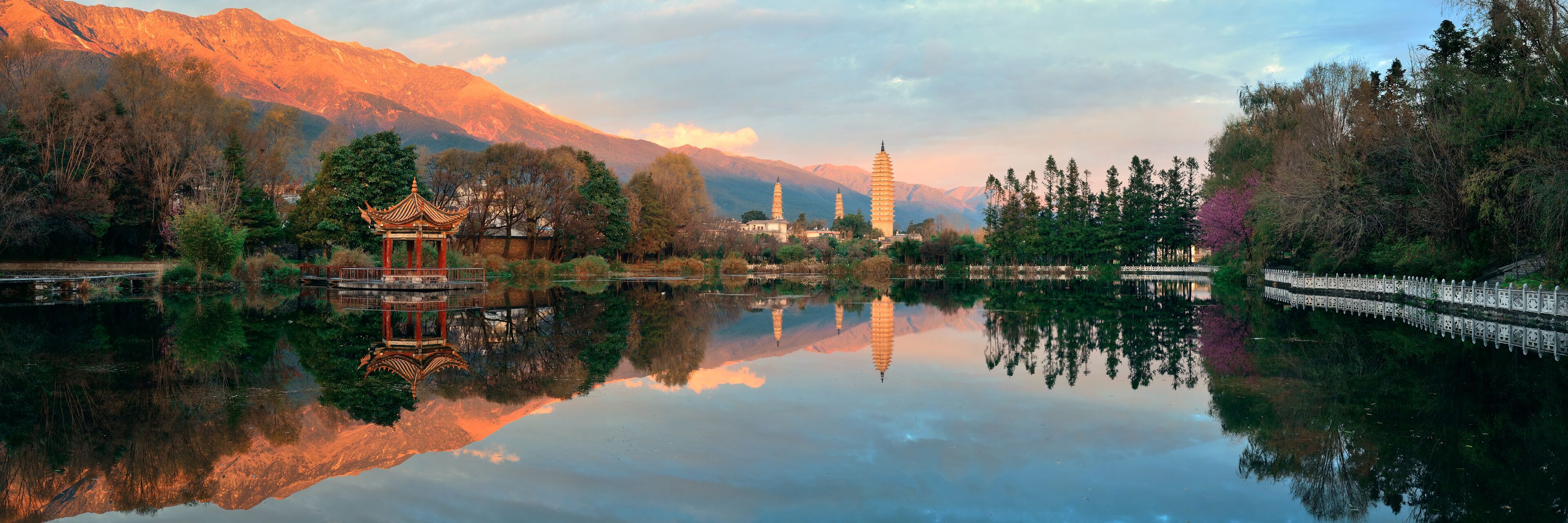 A serene lake with a traditional pavilion, mountains in the background, and a pagoda.