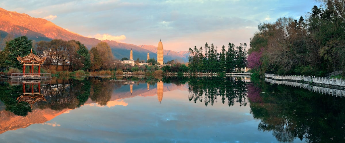 Un lago tranquillo con un padiglione tradizionale, montagne sullo sfondo e una pagoda.