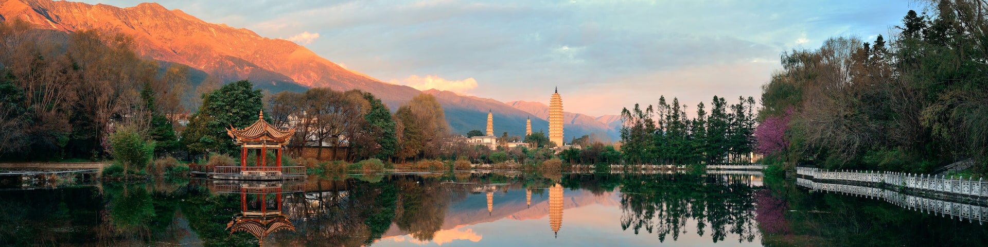 A serene lake with a traditional pavilion, mountains in the background, and a pagoda.