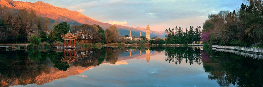 A serene lake with a traditional pavilion, mountains in the background, and a pagoda.