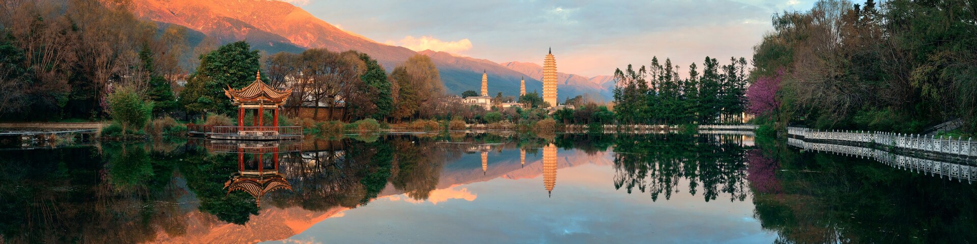 Un lago tranquilo con un pabellón tradicional, montañas al fondo y una pagoda.