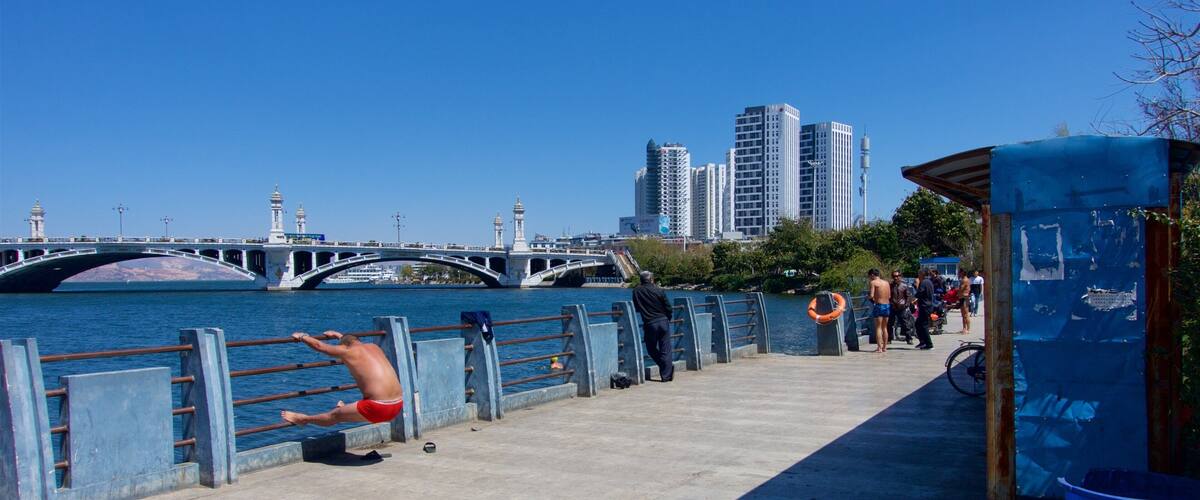 A riverside walkway with a bridge, a mosque, and high-rise buildings in the background.