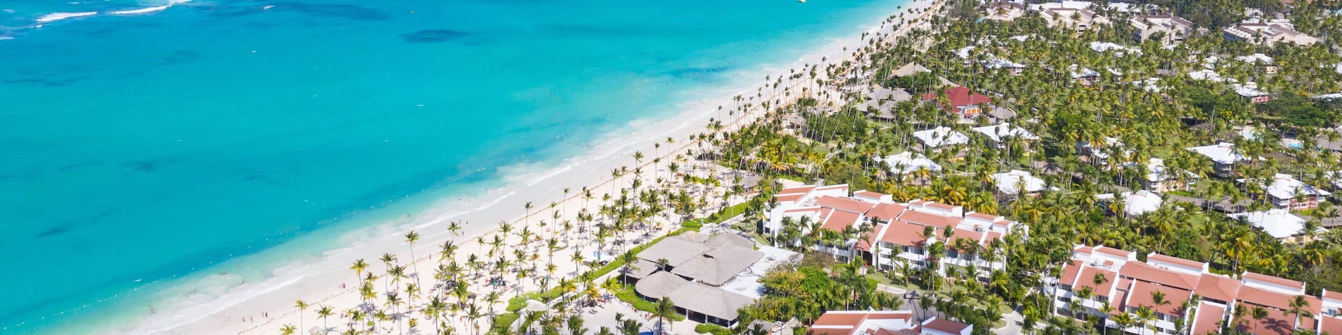 A coastal resort with a beach, palm trees, and a clear blue sea.