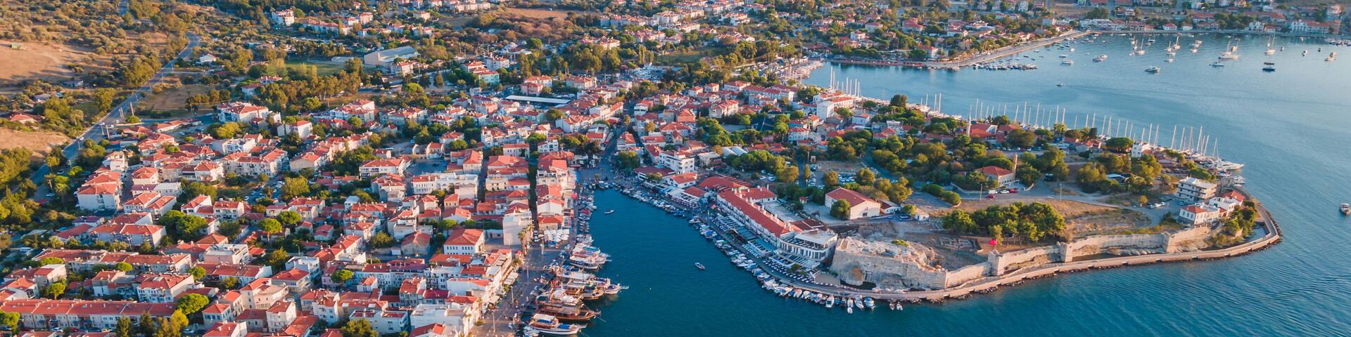 A coastal town with a marina, red-roofed buildings, and a hilly backdrop.