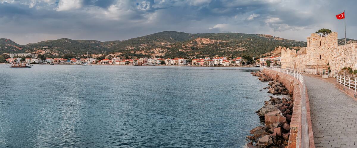 A coastal town with a stone wall, a flag, and boats on the water.