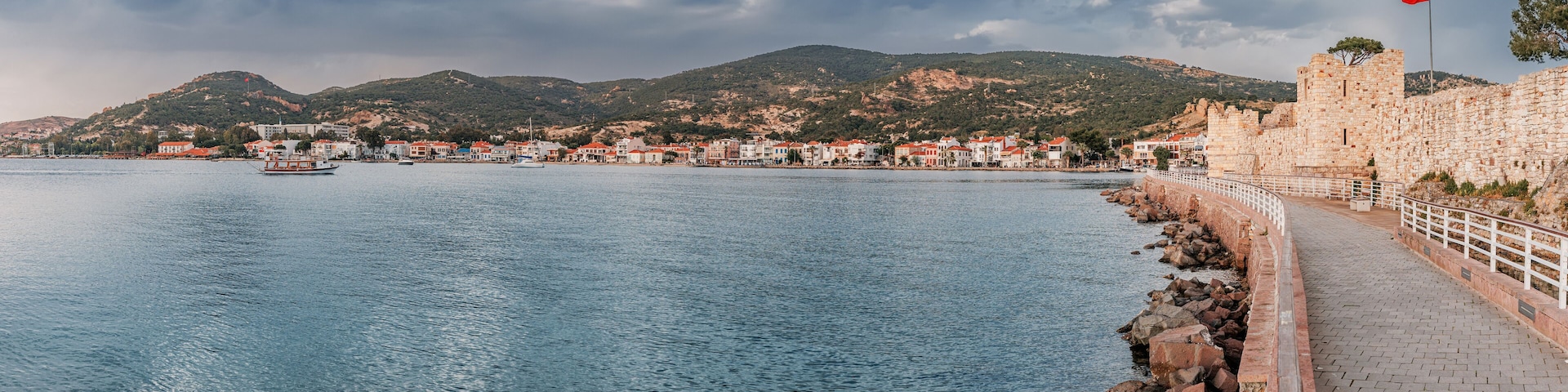 A coastal town with a stone wall, a flag, and boats on the water.