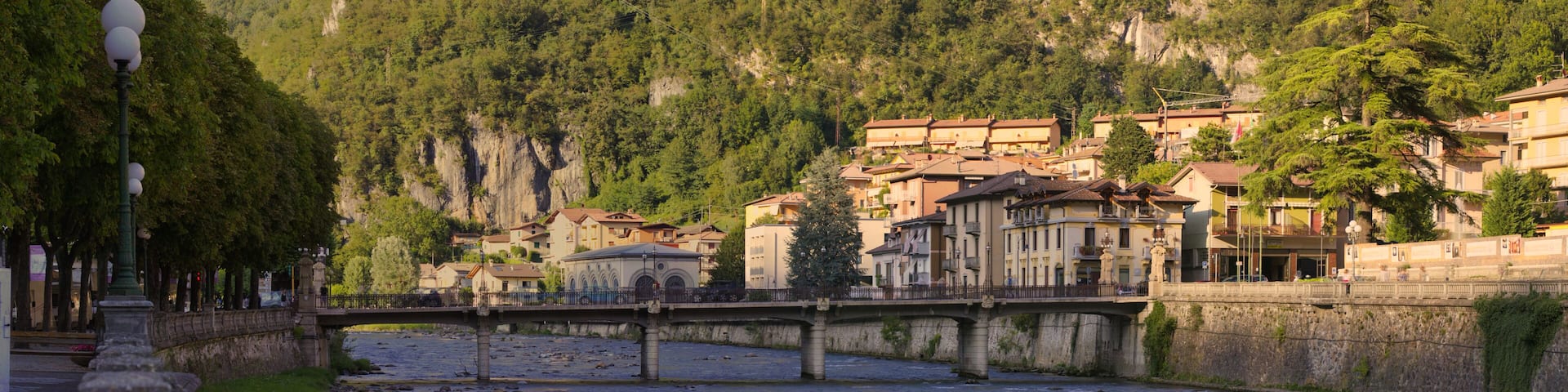 A river with a stone bridge, buildings, and a mountainous backdrop.