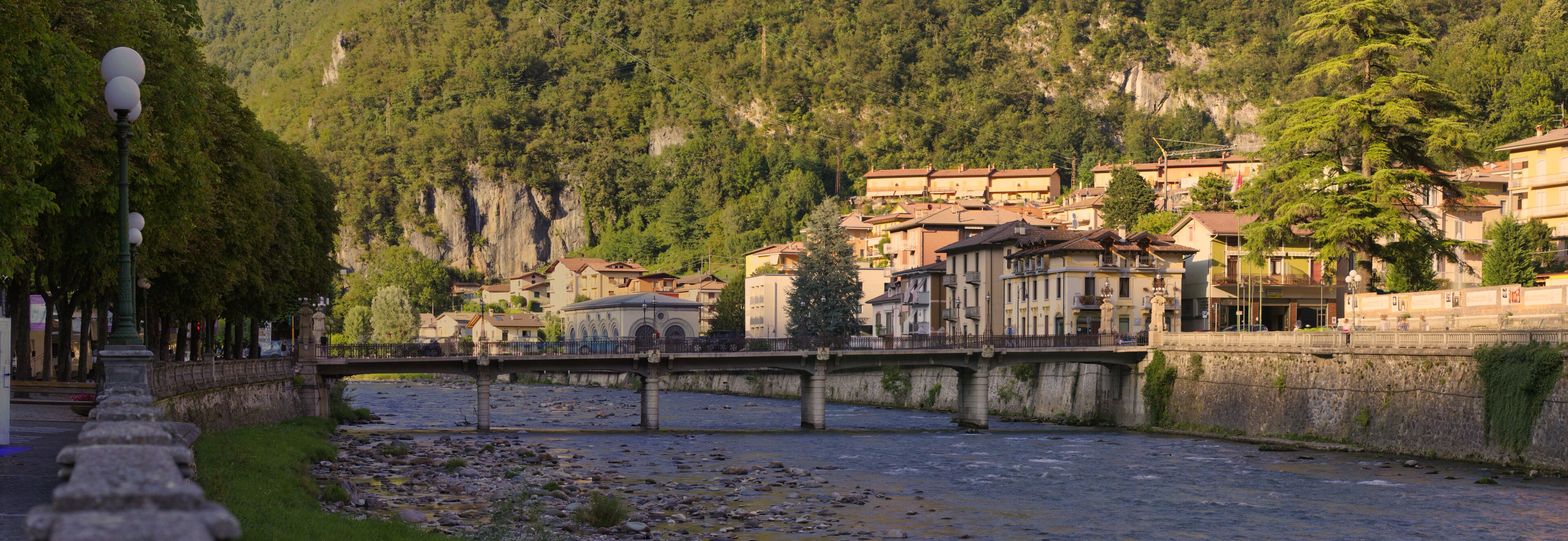 A river with a stone bridge, buildings, and a mountainous backdrop.